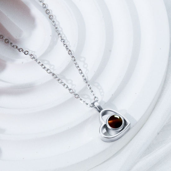 El Collar de corazón con foto, en color plateado, es ideal para collares personalizados y guardar recuerdos especiales. Presentado sobre un fondo blanco texturizado.