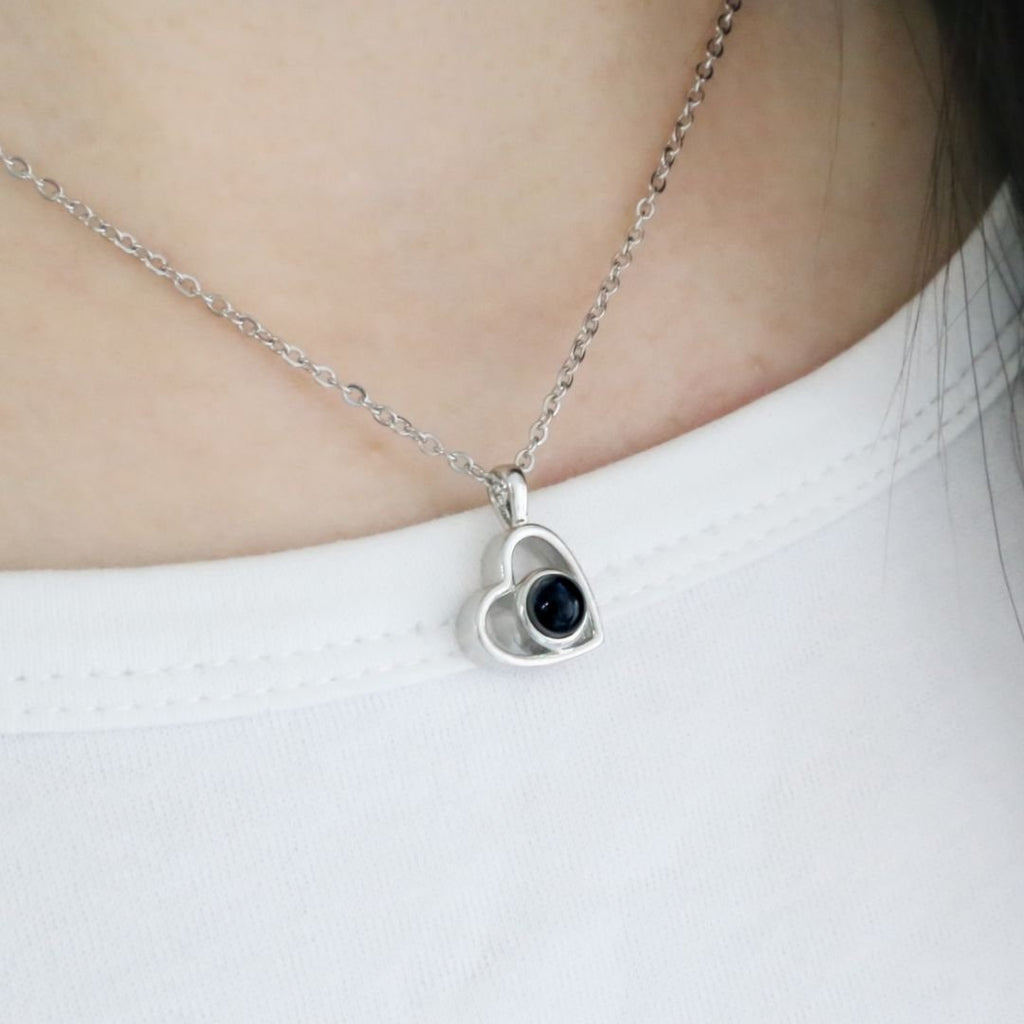 El collar de corazón con foto, con piedra oscura central, es perfecto para guardar recuerdos especiales o como uno de nuestros exclusivos collares personalizados. Ideal para llevar sobre una camisa blanca.