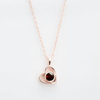 El Collar de corazón con foto es una delicada cadena en oro rosa con colgante en forma de corazón y gema roja, ideal para guardar recuerdos especiales, bellamente presentado sobre fondo blanco.