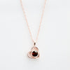 El Collar de corazón con foto es una delicada cadena en oro rosa con colgante en forma de corazón y gema roja, ideal para guardar recuerdos especiales, bellamente presentado sobre fondo blanco.