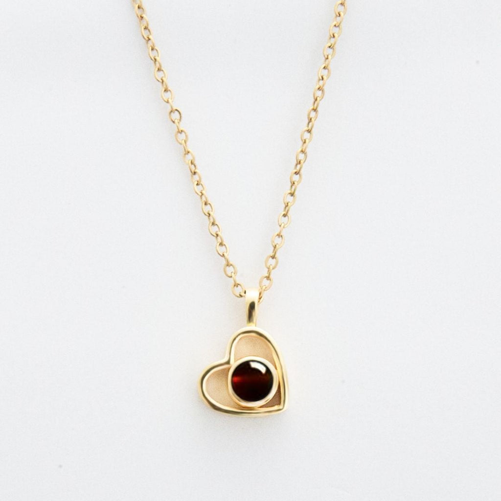 El Collar de corazón con foto es un collar de cadena de oro con un colgante en forma de corazón, con un diseño de contorno abierto y una piedra preciosa redonda de color rojo oscuro: un elegante accesorio para recuerdos especiales, que se muestra sobre un fondo blanco.
