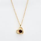 El Collar de corazón con foto es un collar de cadena de oro con un colgante en forma de corazón, con un diseño de contorno abierto y una piedra preciosa redonda de color rojo oscuro: un elegante accesorio para recuerdos especiales, que se muestra sobre un fondo blanco.