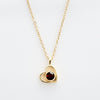 El Collar de corazón con foto es un collar de cadena de oro con un colgante en forma de corazón, con un diseño de contorno abierto y una piedra preciosa redonda de color rojo oscuro: un elegante accesorio para recuerdos especiales, que se muestra sobre un fondo blanco.