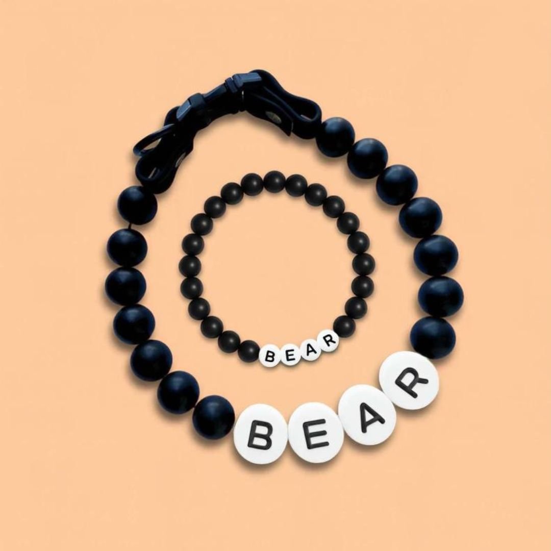 El Collar de cuentas personalizado para mascotas + Pulsera gratis se muestra con cuentas negras y grandes letras blancas BEAR sobre fondo durazno, ideal como regalo para amantes de mascotas o pulsera a juego para tu amigo peludo.