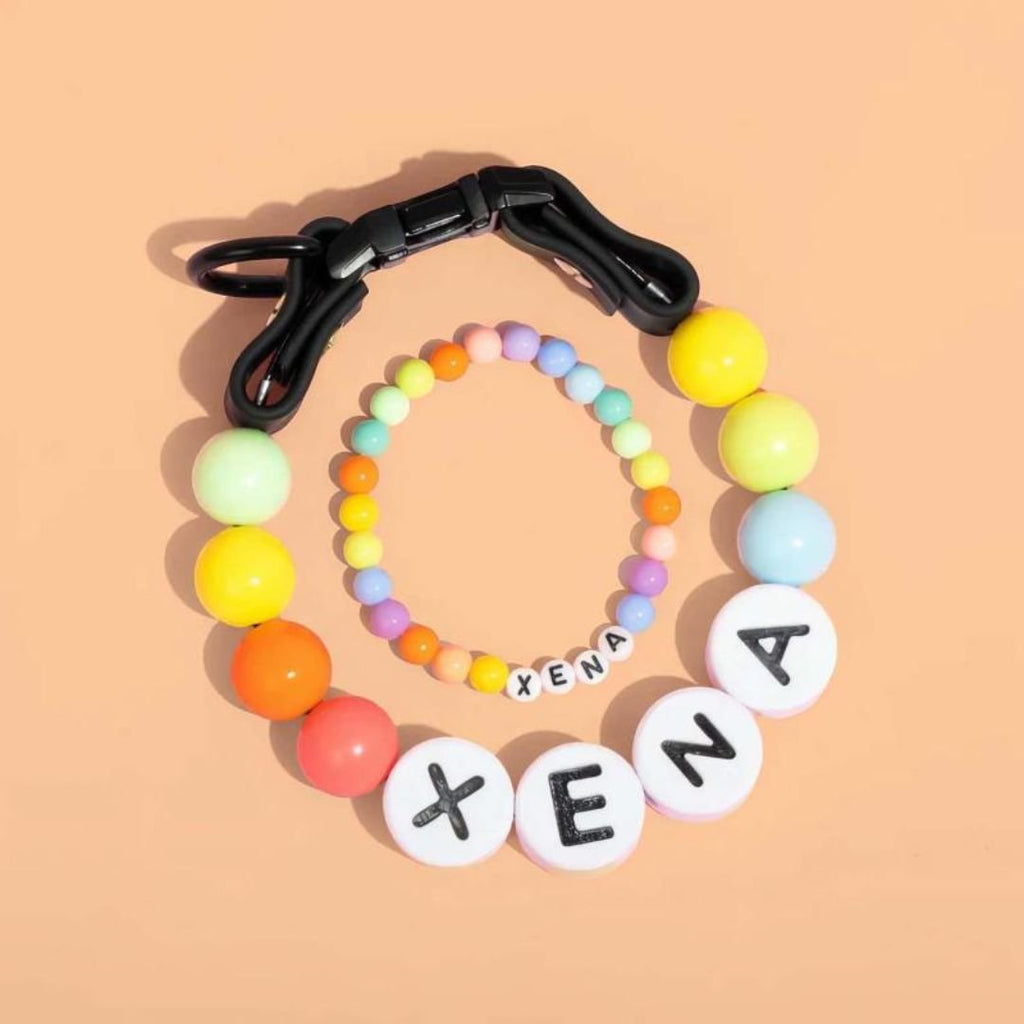 Collar de cuentas personalizado para mascotas + pulsera gratis en fondo durazno, con cuentas redondas y grandes letras blancas "XENA", ideal como regalo para amantes de mascotas.