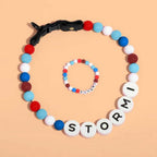 Un collar de cuentas personalizado para mascotas y una pulsera a juego, ambos con cuentas de letras redondas que deletrean STORMI, mostradas sobre un fondo melocotón.