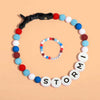 Un collar de cuentas personalizado para mascotas y una pulsera a juego, ambos con cuentas de letras redondas que deletrean STORMI, mostradas sobre un fondo melocotón.