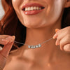 Una mujer sonriente con labios brillantes sostiene un delicado Collar de huellitas de mascotas personalizado cerca de la cara, resaltando los detalles únicos de pepitas metálicas de esta joya personalizada.