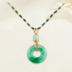El collar de piedra jade esmeralda natural, con una cadena de cuentas verdes y doradas y un colgante redondo de jade con acento dorado y piedra preciosa, luce con elegancia sobre un fondo neutro.
