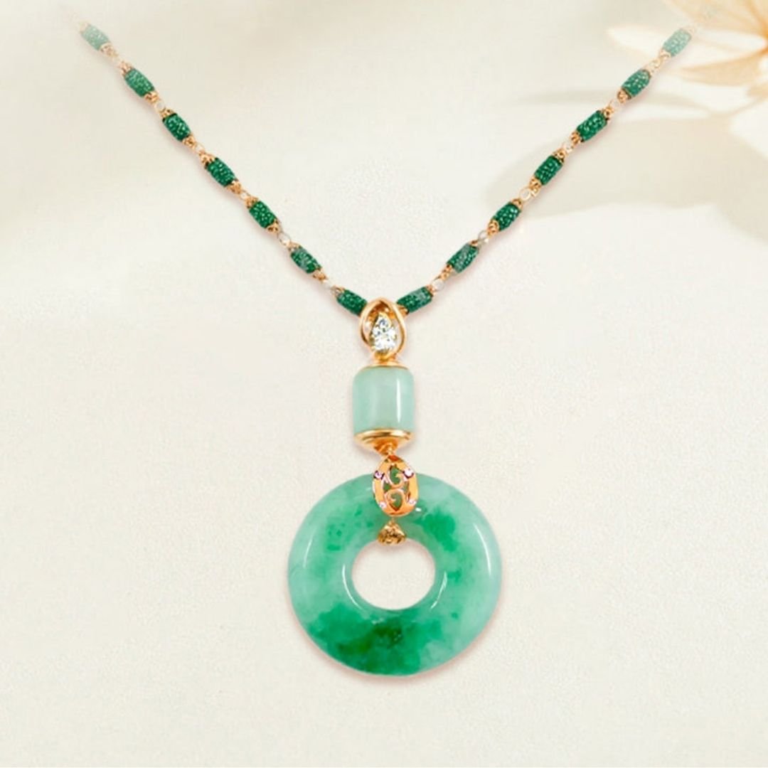 El collar de piedra jade esmeralda natural, con una cadena de cuentas verdes y doradas y un colgante redondo de jade con acento dorado y piedra preciosa, luce con elegancia sobre un fondo neutro.