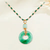 El collar de piedra jade esmeralda natural, con una cadena de cuentas verdes y doradas y un colgante redondo de jade con acento dorado y piedra preciosa, luce con elegancia sobre un fondo neutro.