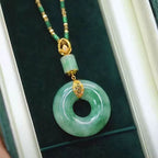 El collar de piedra jade esmeralda natural incluye un colgante circular de jade y una cuenta cilíndrica con detalles dorados, bellamente presentados en un joyero de color verde oscuro: una impresionante pieza de joyería de jade natural.