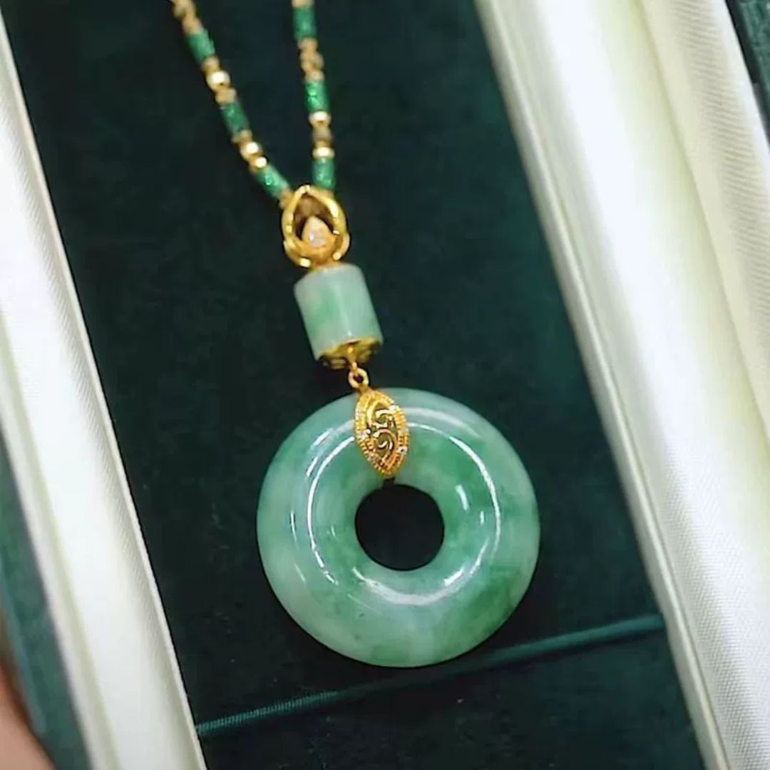 El collar de piedra jade esmeralda natural incluye un colgante circular de jade y una cuenta cilíndrica con detalles dorados, bellamente presentados en un joyero de color verde oscuro: una impresionante pieza de joyería de jade natural.