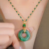 A Collar de piedra jade esmeralda natural con cuentas verdes y detalles dorados luce un colgante circular de jade y una pequeña cuenta cilíndrica. Una mano acaricia el acabado brillante de esta joyería auténtica.