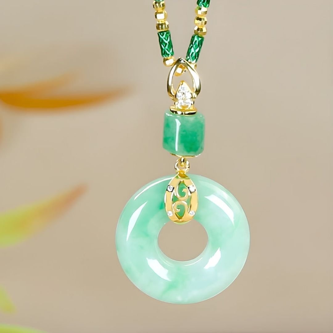 El collar de piedra jade esmeralda natural presenta un colgante en forma de donut de jade verde con detalles de oro y diamantes, suspendido de un cordón decorativo verde y dorado, sobre un fondo neutro.
