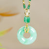 El collar de piedra jade esmeralda natural presenta un colgante en forma de donut de jade verde con detalles de oro y diamantes, suspendido de un cordón decorativo verde y dorado, sobre un fondo neutro.