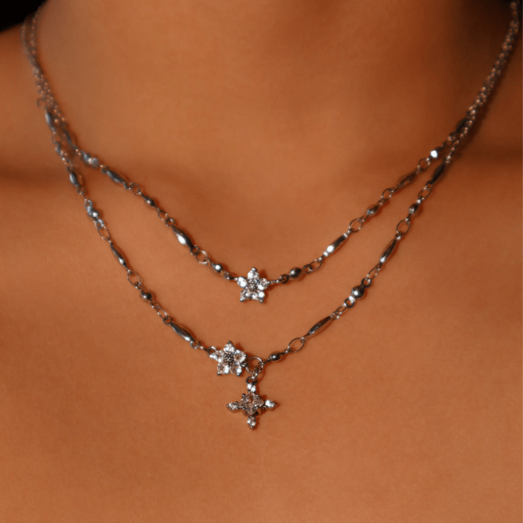 Primer plano del cuello de una persona que lleva dos collares de plata en capas, uno de los cuales es el Collar Destello de estrella. Ambos llevan delicados colgantes en forma de estrella adornados con piedras brillantes.