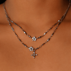 Primer plano del cuello de una persona que lleva dos collares de plata en capas, uno de los cuales es el Collar Destello de estrella. Ambos llevan delicados colgantes en forma de estrella adornados con piedras brillantes.