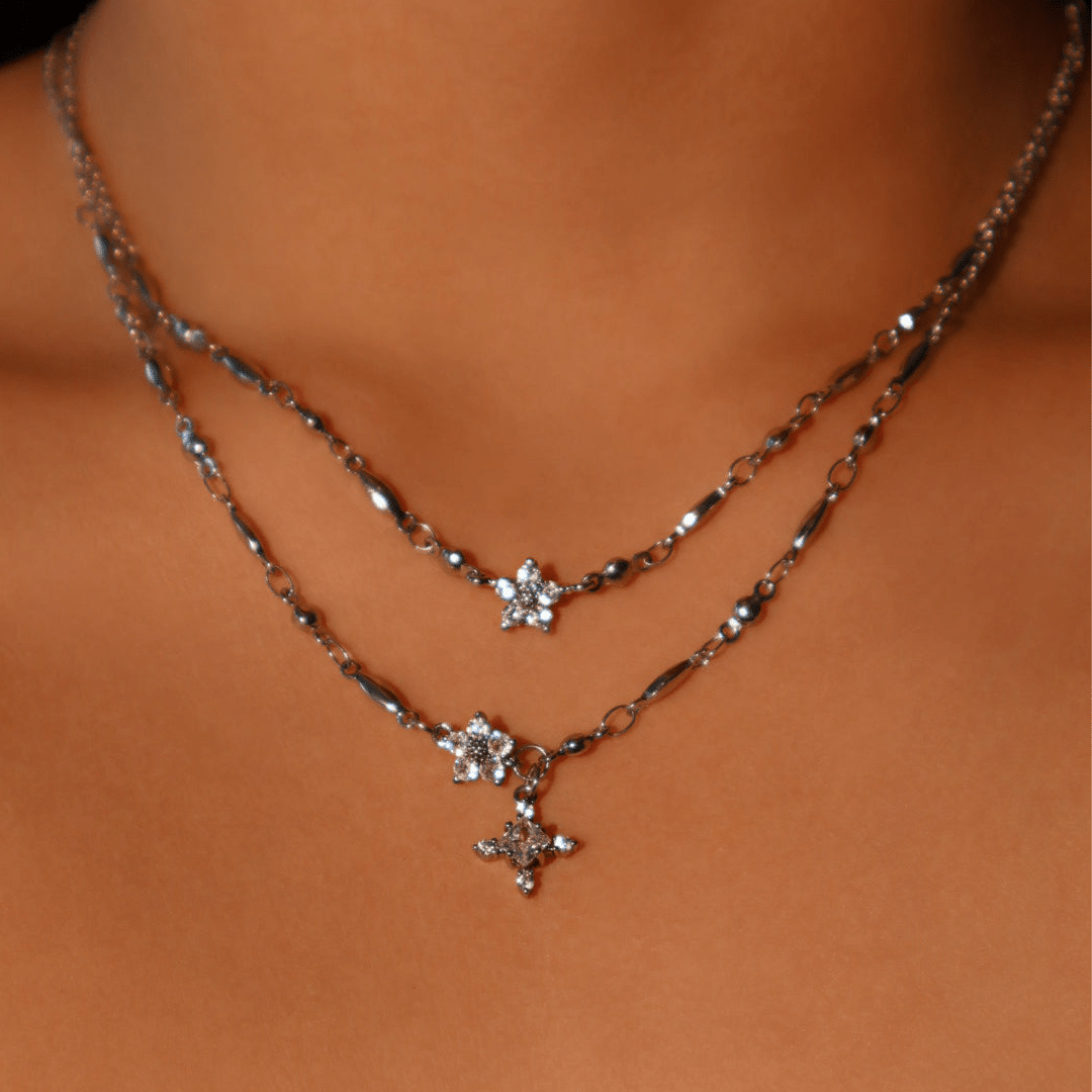 Primer plano del cuello de una persona que lleva dos collares de plata en capas, uno de los cuales es el Collar Destello de estrella. Ambos llevan delicados colgantes en forma de estrella adornados con piedras brillantes.