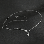El collar Destello de estrella es un delicado collar de plata con una fina cadena, pequeños eslabones decorativos y un colgante en forma de estrella acentuado con piedras brillantes, que se muestra sobre una superficie negra texturizada.