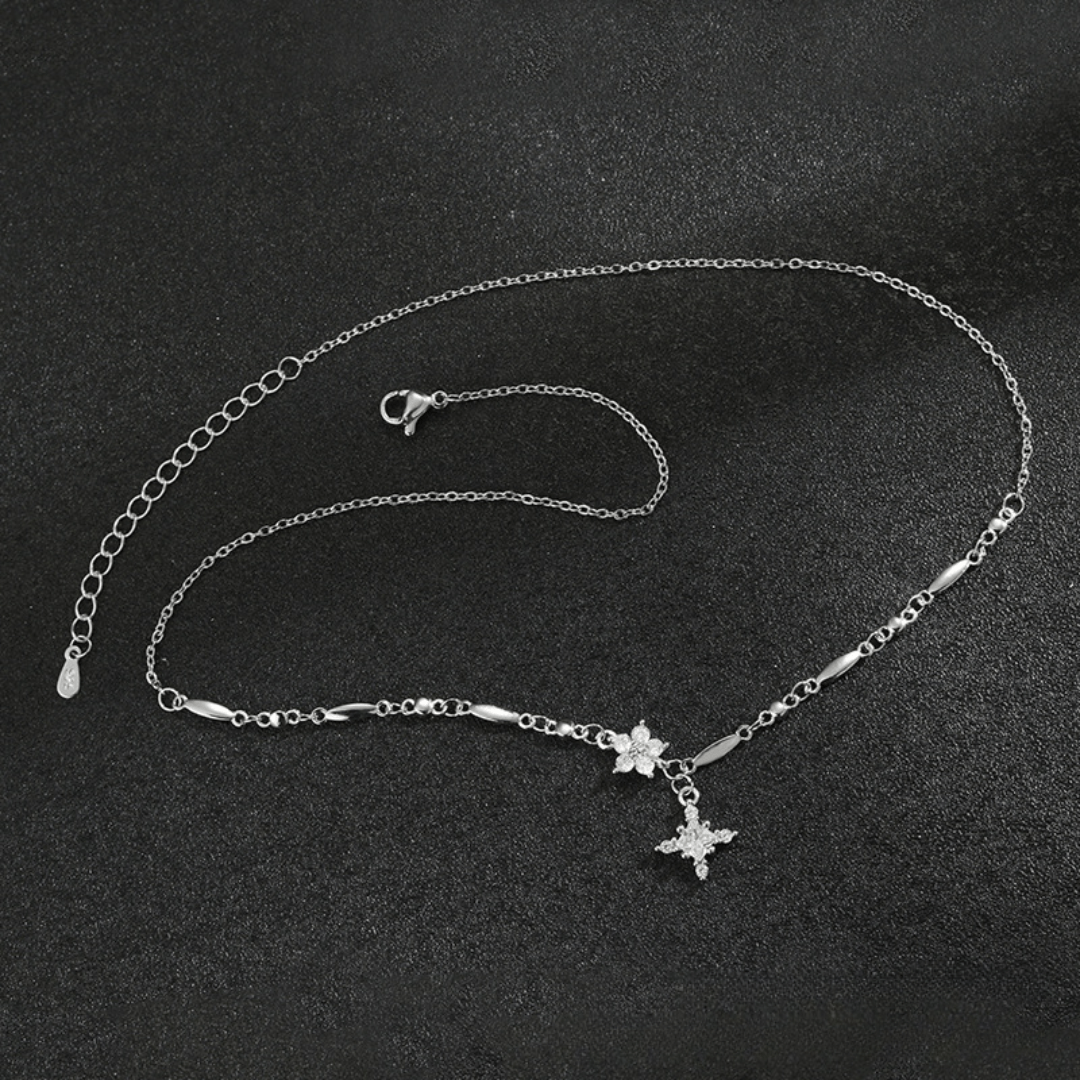El collar Destello de estrella es un delicado collar de plata con una fina cadena, pequeños eslabones decorativos y un colgante en forma de estrella acentuado con piedras brillantes, que se muestra sobre una superficie negra texturizada.