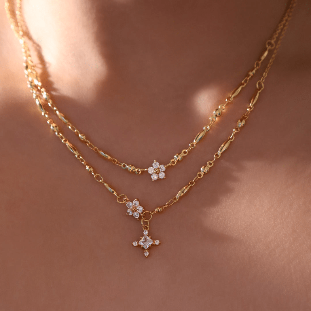Un primer plano del cuello de una persona muestra collares de cadena de oro en capas, incluido el Collar Destello de estrella, con cada colgante adornado con pequeñas piedras brillantes sobre una piel suavemente iluminada.