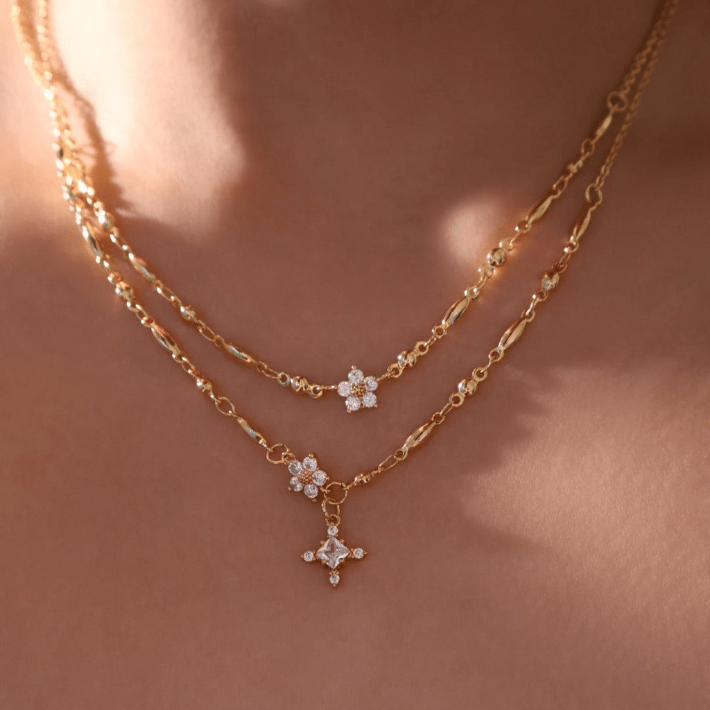 Un primer plano del cuello de una persona muestra collares de cadena de oro en capas, incluido el Collar Destello de estrella, con cada colgante adornado con pequeñas piedras brillantes sobre una piel suavemente iluminada.