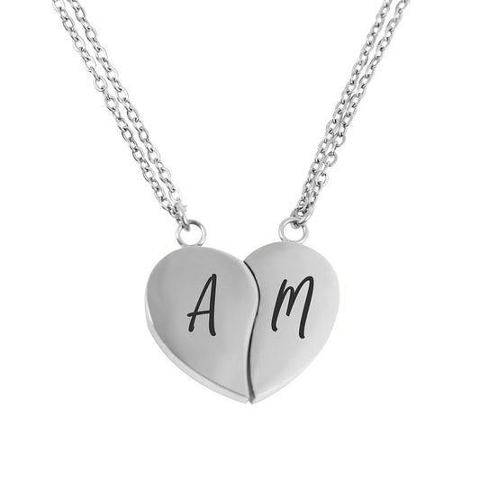 El Collar Dúo medio corazón, color plateado, incluye dos collares con un dije de corazón partido y letras A y M grabadas en negro-el regalo ideal para parejas.