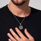 Una persona con camisa negra muestra el collar Estrella del Norte - Para mi hijo (con nota dedicada), con un colgante circular plateado y detallado, un regalo ideal para un hijo.