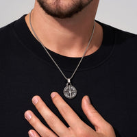 Una persona con camisa negra muestra el collar Estrella del Norte - Para mi hijo (con nota dedicada), con un colgante circular plateado y detallado, un regalo ideal para un hijo.