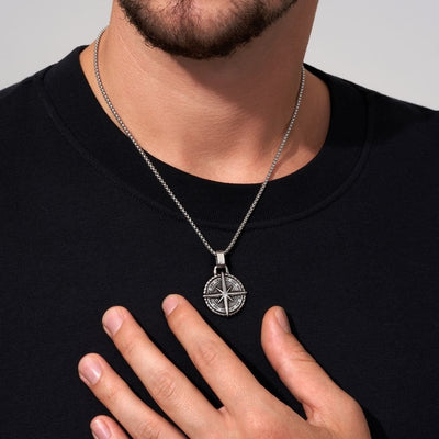 Una persona con camisa negra muestra el collar Estrella del Norte - Para mi hijo (con nota dedicada), con un colgante circular plateado y detallado, un regalo ideal para un hijo.