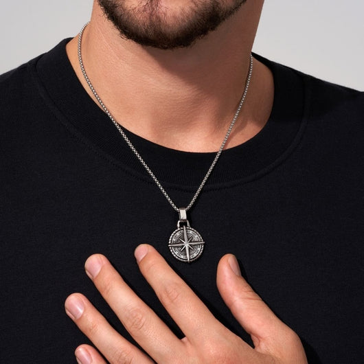 Una persona con camisa negra muestra el collar Estrella del Norte - Para mi hijo (con nota dedicada), con un colgante circular plateado y detallado, un regalo ideal para un hijo.