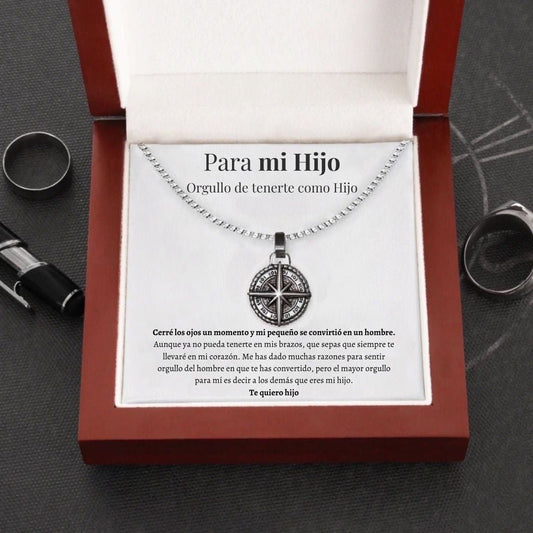 El collar Estrella del Norte - Para mi hijo (con nota dedicada) se presenta en una caja roja abierta con una cariñosa nota en español para un hijo, que expresa orgullo y amor. Rodeado de anillos y un bolígrafo sobre una superficie oscura, es un regalo lleno de significado.