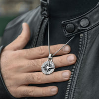 Una persona con chaqueta de cuero negra sostiene el Collar Estrella del Norte - Para mi hijo (con nota dedicada), con un detallado diseño de brújula y marcas grabadas, que lo convierten en un significativo regalo para hijo.