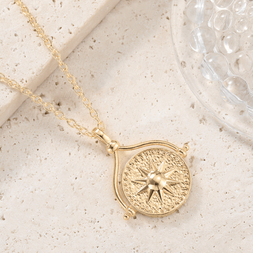 Collar giratorio Sol y Luna "Hatha" con dije circular texturizado y estrella en relieve, expuesto sobre una piedra beige claro junto a un objeto decorativo transparente.