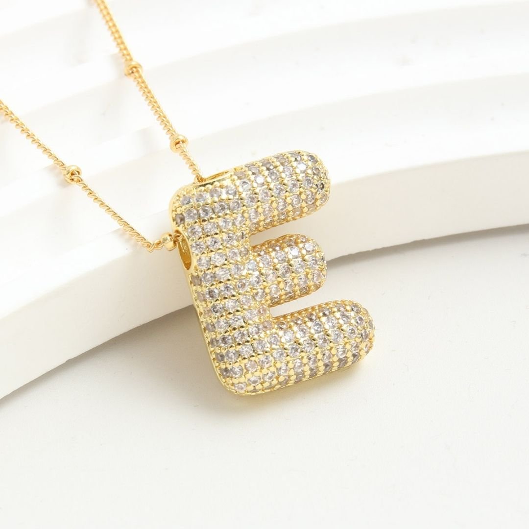 El Collar Inicial Bubble, ahora en oferta de 2x1, presenta una gran letra E mayúscula cubierta de brillantes strass. Un collar dorado y personalizado, perfecto para regalar.