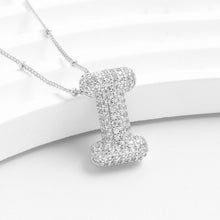 Cargar imagen en el visor de la galería, The Collar Inicial Bubble - ¡Llévate 2 por el precio de 1! luce un colgante con forma de letra I, decorado con brillantes cristales transparentes y exhibido sobre una elegante superficie blanca y curva.