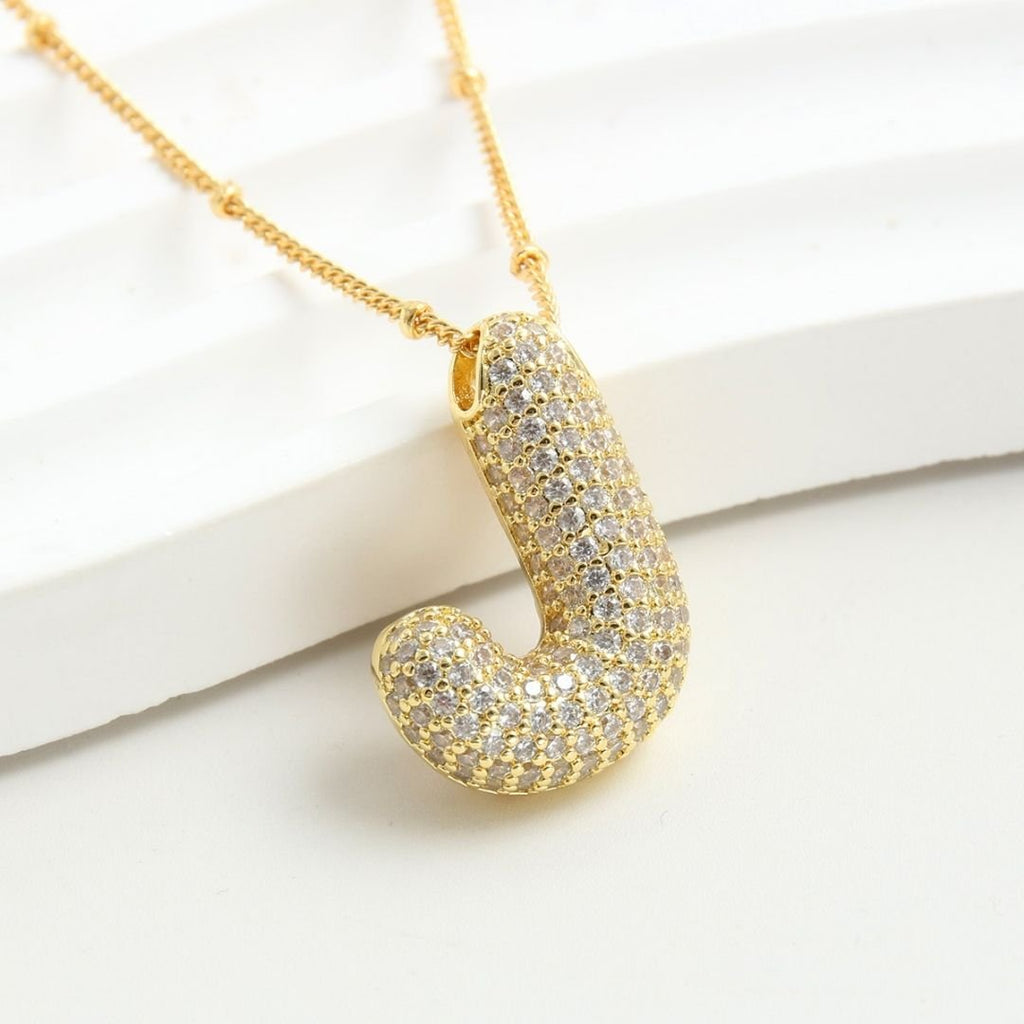 El Collar Inicial Bubble - ¡Llévate 2 por el precio de 1! es un collar dorado con J inicial y piedras brillantes, ideal como collar personalizado y regalo especial, presentado sobre fondo blanco.