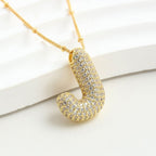 El Collar Inicial Bubble - ¡Llévate 2 por el precio de 1! es un collar dorado con J inicial y piedras brillantes, ideal como collar personalizado y regalo especial, presentado sobre fondo blanco.