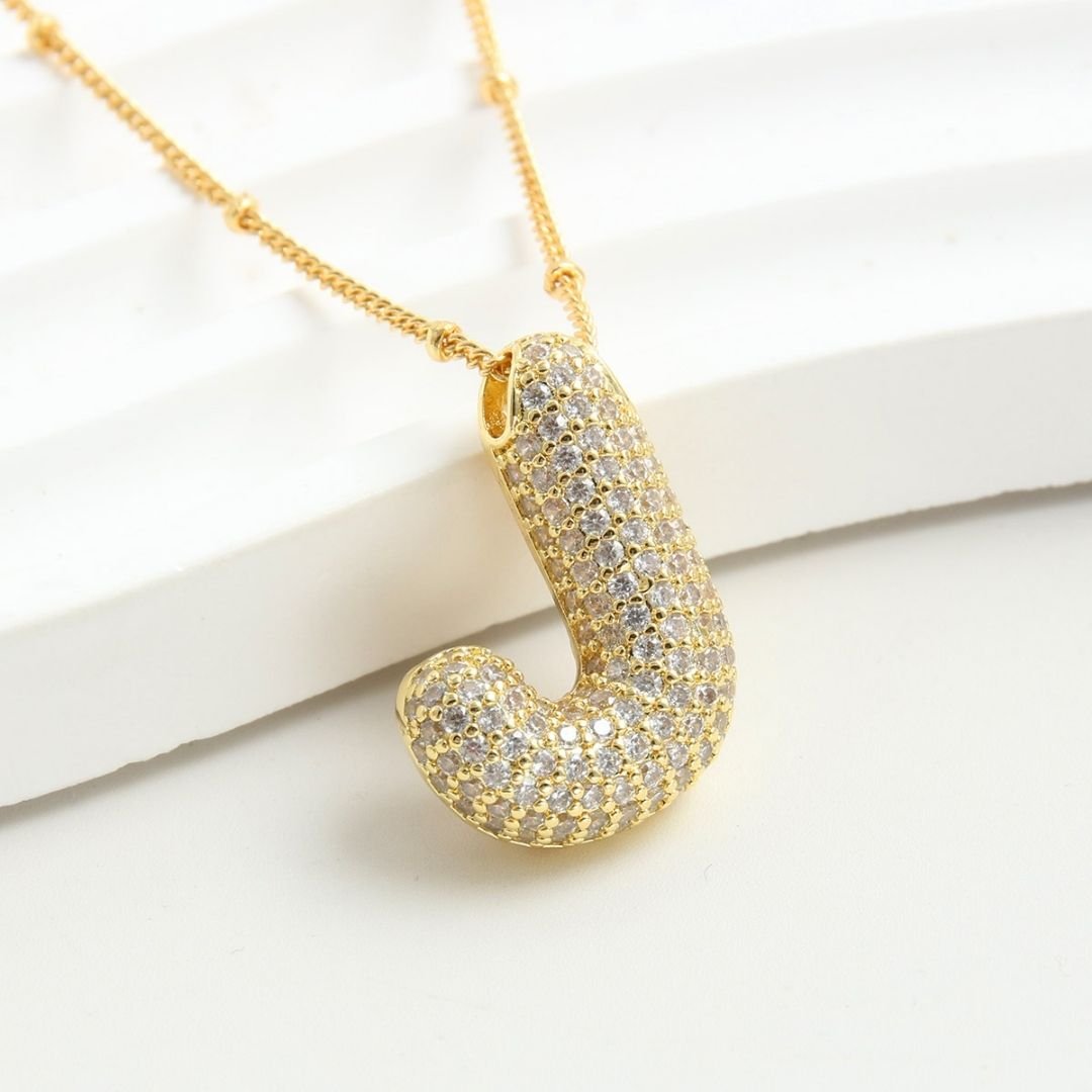 El Collar Inicial Bubble - ¡Llévate 2 por el precio de 1! es un collar dorado con J inicial y piedras brillantes, ideal como collar personalizado y regalo especial, presentado sobre fondo blanco.