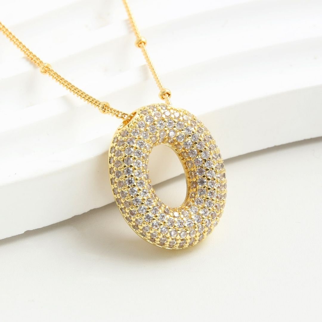 The Collar Inicial Bubble-¡Llévate 2 por el precio de 1!-es un elegante collar personalizado, ideal como regalo especial, con un colgante inicial estilizado que resalta sobre cualquier superficie blanca.