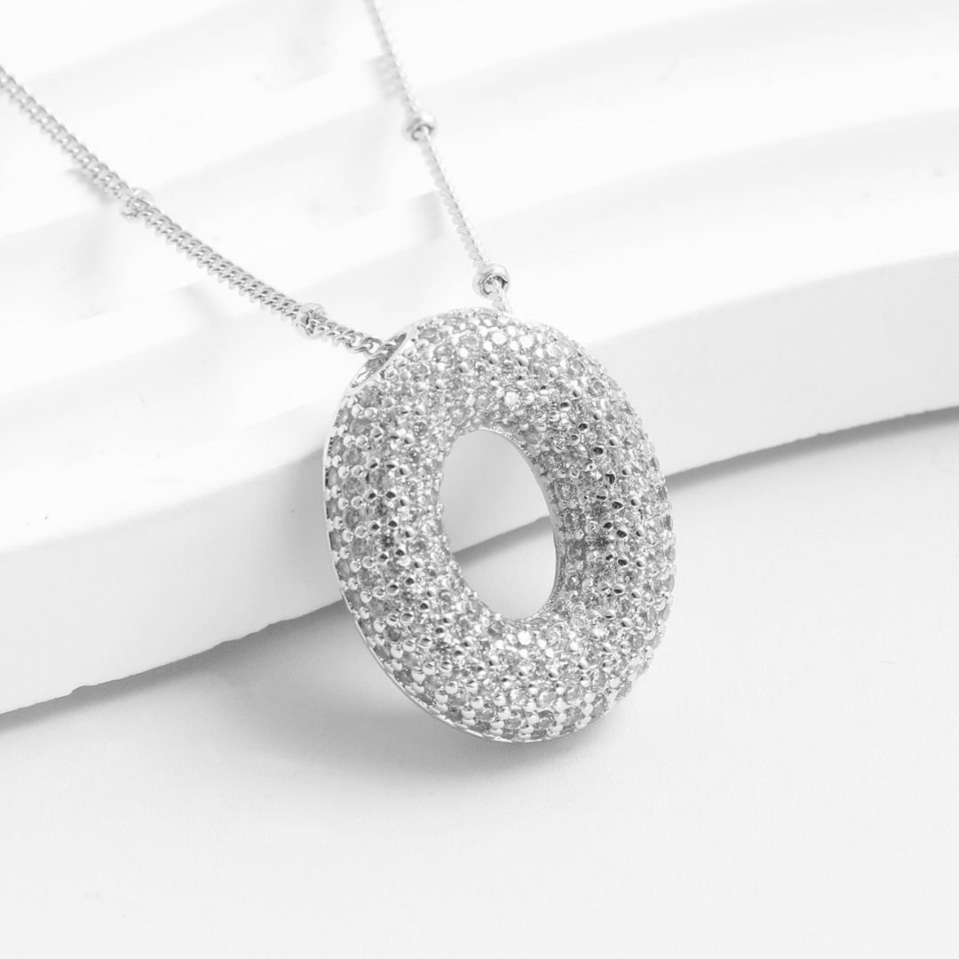 El Collar Inicial Bubble, con dije redondo y cristales brillantes, se muestra sobre una superficie blanca. ¡Llévate 2 por el precio de 1! Ideal como regalo personalizado.