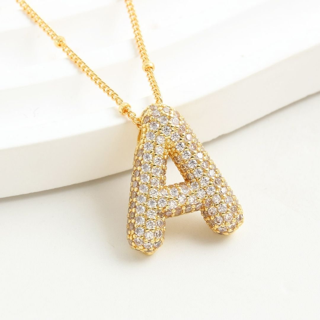 Collar Inicial Bubble: cadena dorada con dije de letra A decorado con brillantes, sobre fondo blanco. ¡Llévate 2 por el precio de 1! Un collar elegante y personalizado, ideal para regalar.