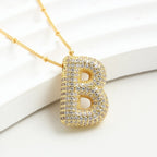 El Collar Inicial Bubble - ¡Llévate 2 por el precio de 1! es un collar dorado con dije grande de letra "B" cubierto de brillantes, exhibido sobre fondo blanco texturizado-un regalo personalizado perfecto.