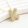 El Collar Inicial Bubble - ¡Llévate 2 por el precio de 1! es un collar dorado con inicial y brillantes, exhibido sobre fondo blanco texturizado; ideal como regalo personalizado para alguien especial.