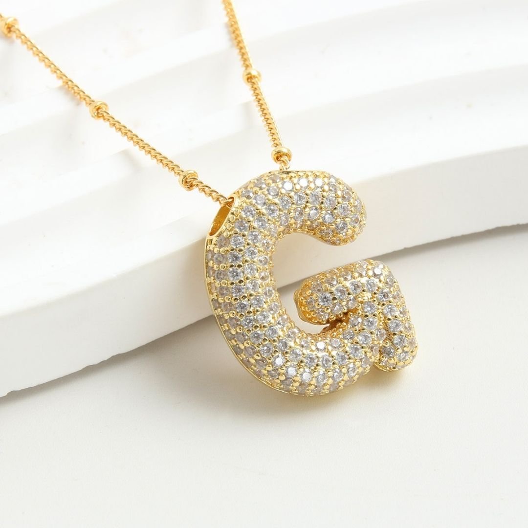 El Collar Inicial Bubble luce una gran letra inicial G con cristales brillantes sobre fondo blanco texturizado. ¡Lévate 2 por el precio de 1 y crea el regalo personalizado perfecto!.