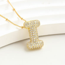 Cargar imagen en el visor de la galería, The Collar Inicial Bubble - ¡Llévate 2 por el precio de 1! es un collar dorado con dije de inicial, incrustado con cristales claros sobre fondo blanco texturizado, ideal como collar personalizado o regalo especial.