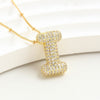 The Collar Inicial Bubble - ¡Llévate 2 por el precio de 1! es un collar dorado con dije de inicial, incrustado con cristales claros sobre fondo blanco texturizado, ideal como collar personalizado o regalo especial.