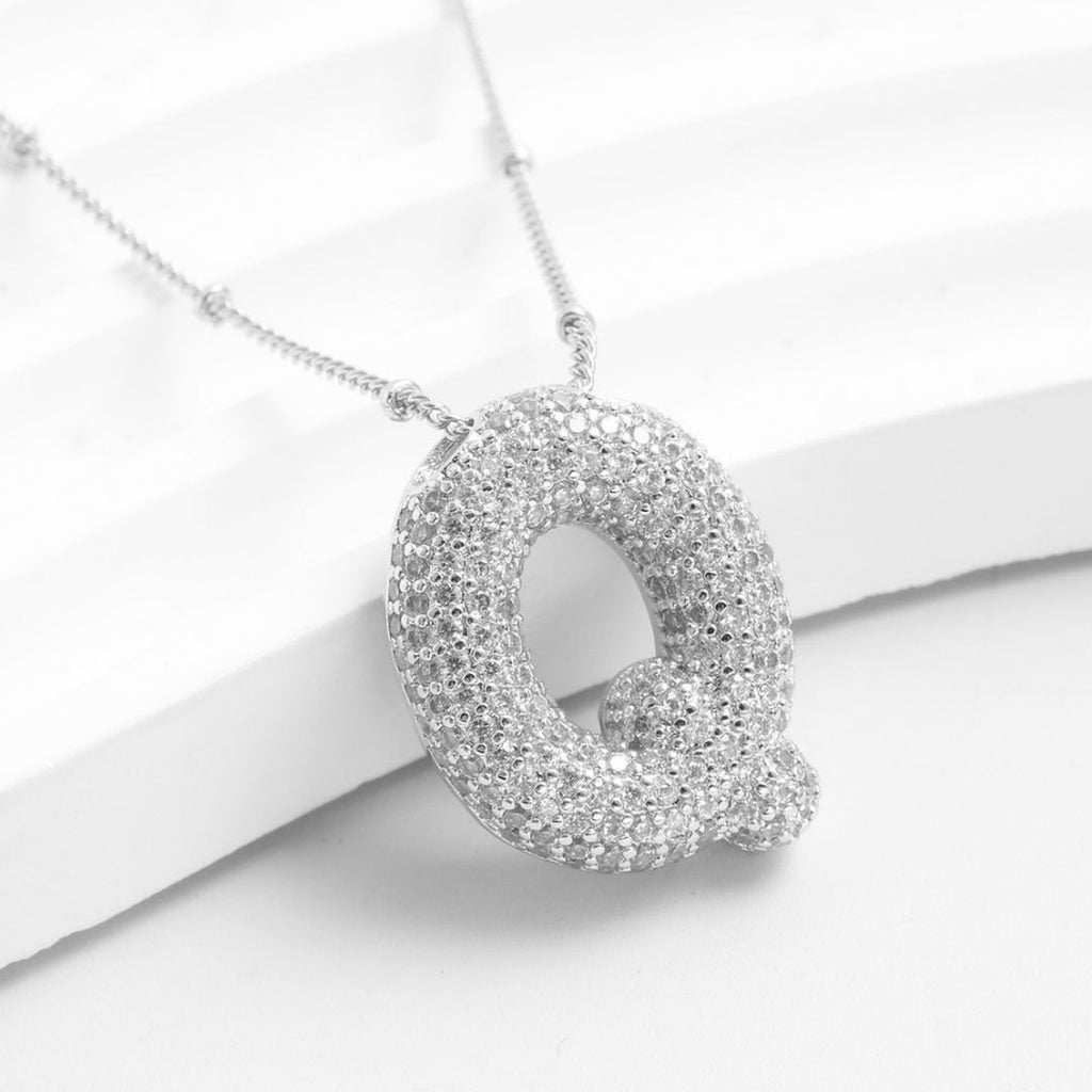 The Collar Inicial Bubble - ¡Llévate 2 por el precio de 1! es un collar plateado con inicial Q y brillantes piedras claras, perfecto como regalo personalizado. Se muestra sobre fondo blanco.