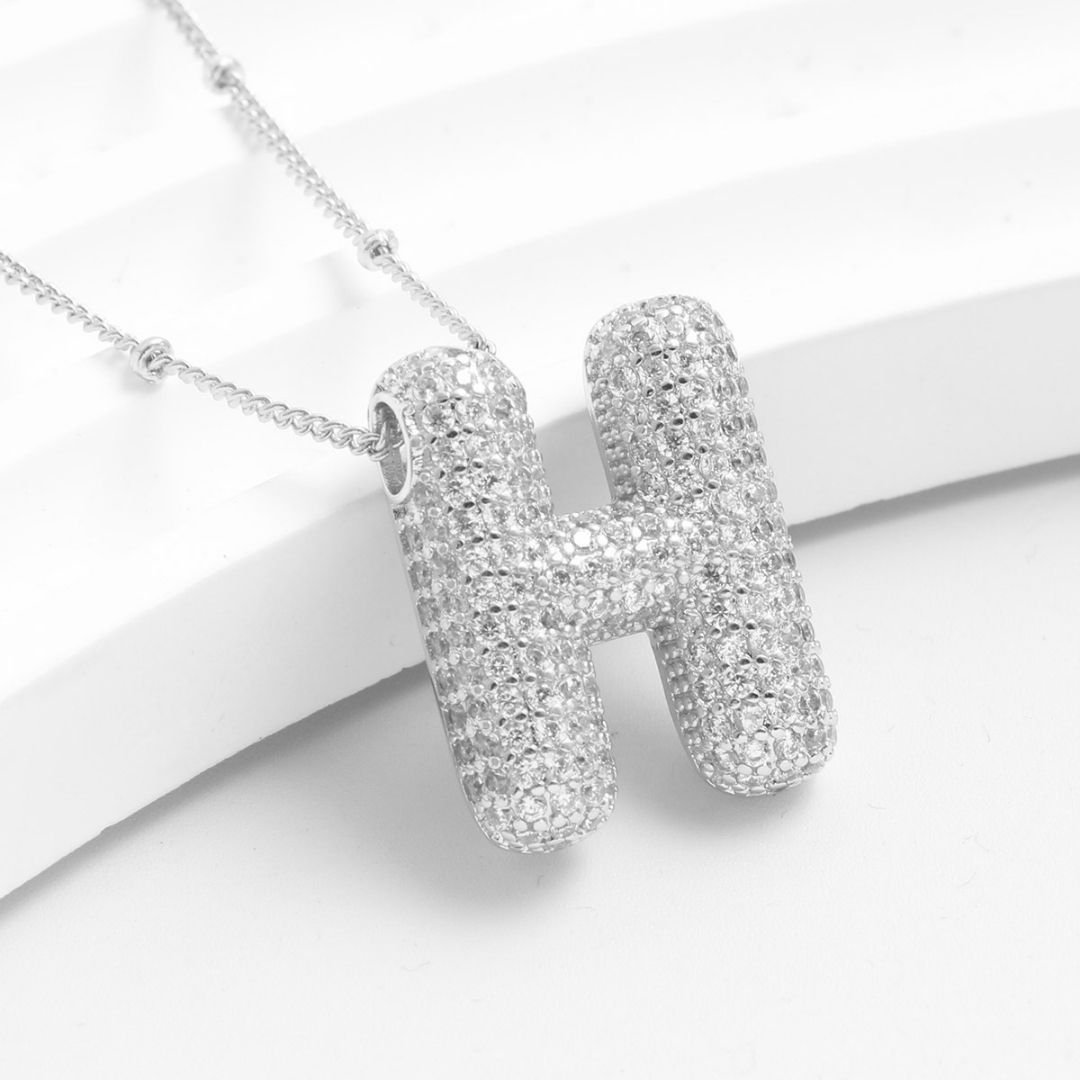 El collar Inicial Bubble - ¡Llévate 2 por el precio de 1! se presenta en plata con la H inicial y cristales brillantes sobre fondo blanco. Es una opción personalizada perfecta para regalar en ocasiones especiales.